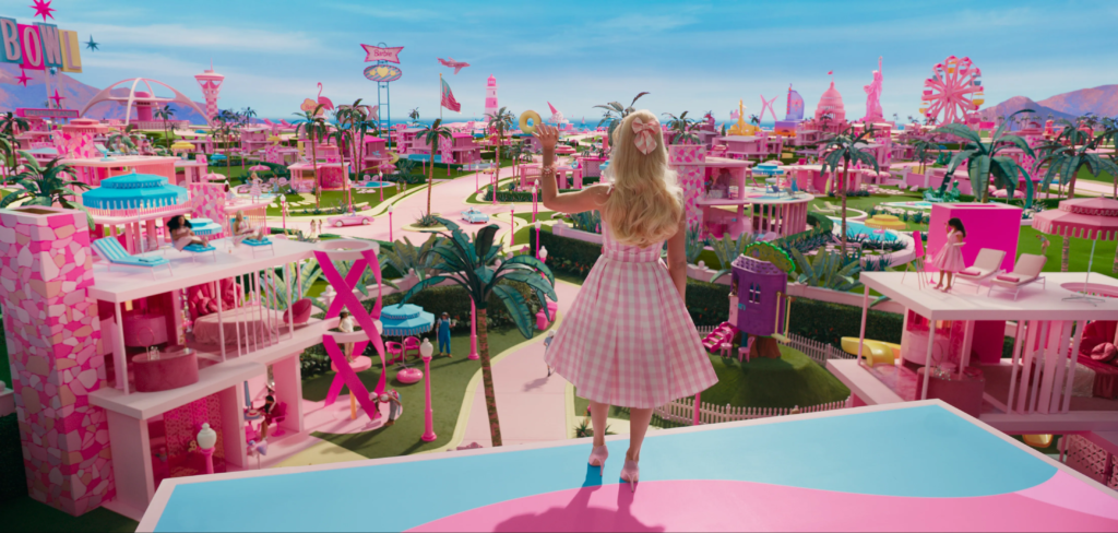 screen grab from the Barbie 2023 trailer, depicts Barbie waving at the bright pink city